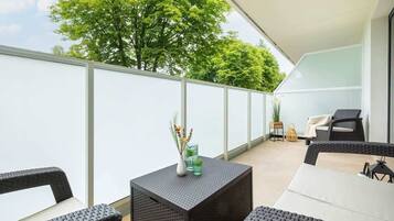 Ein Balkon mit Korbmöbeln, einem kleinen Tisch mit einer Vase und einem Stuhl.