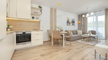 Eine moderne Küche mit integrierten Geräten, ein Essbereich mit Tisch und Stühlen, eine Couch und ein großes Fenster mit Vorhängen.