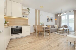 A modern kitchen with built-in appliances, a dining area with a table and chairs, a sofa, and a large window with curtains.
