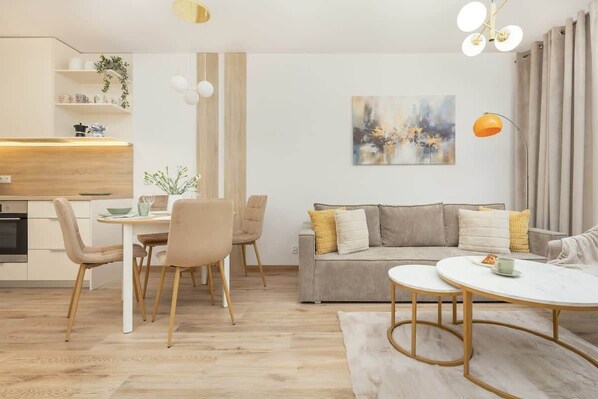 A modern living room with a sofa, dining table, chairs, and a kitchen area.