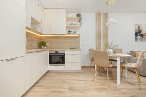 A modern kitchen with white cabinetry, a built-in oven, and a dining area with a table and chairs.