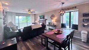 Una sala de estar acogedora con un sofá de color oscuro, una mesa de comedor de madera con individuales rosa y un ventilador de techo.