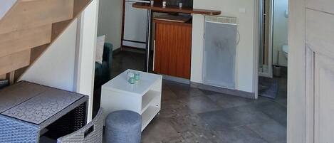 A multi-level interior with a wooden staircase, a kitchen area, and a seating area with a small table and ottoman.
