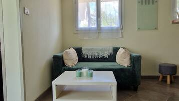 A room with a green sofa, a white table with candles, and a window with sheer curtains.