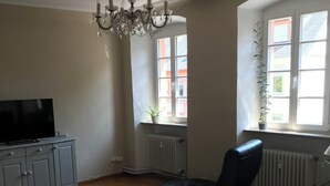 En stue med en hvid sofa, en sort lænestol, et glasbord, et fjernsyn på et skab og en lysekrone.