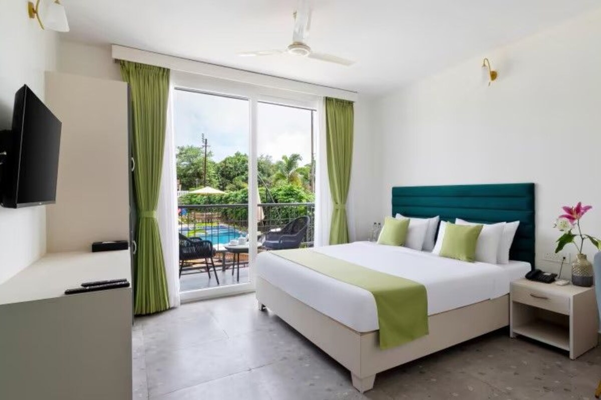 A hotel room with a bed, a desk, a chair, a TV, and a balcony with a pool.
