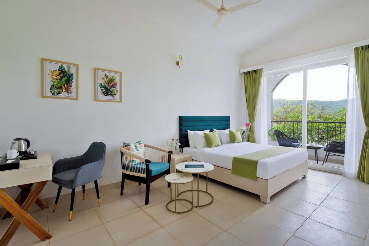 Habitación de hotel con cama, escritorio, silla, mesita y balcón con vistas.