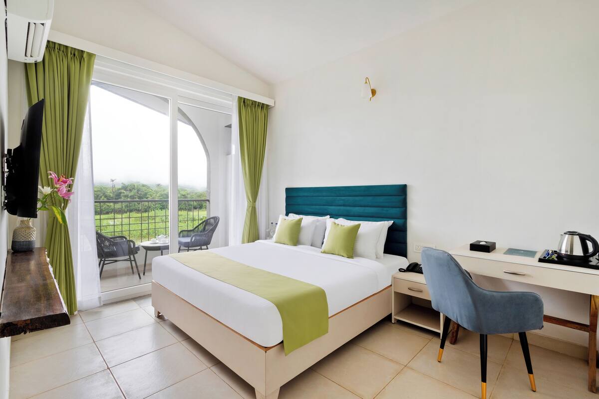 Habitación de hotel con cama, escritorio, una silla y vista a zonas verdes.