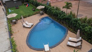 A swimming pool with lounge chairs and umbrellas, surrounded by greenery and a slide. - Stone Wood Hotel Amboli (Sawantwadi)