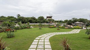 A well-maintained garden with a curved stone pathway, benches, and various plants. - Stone Wood Hotel Amboli (Sawantwadi)