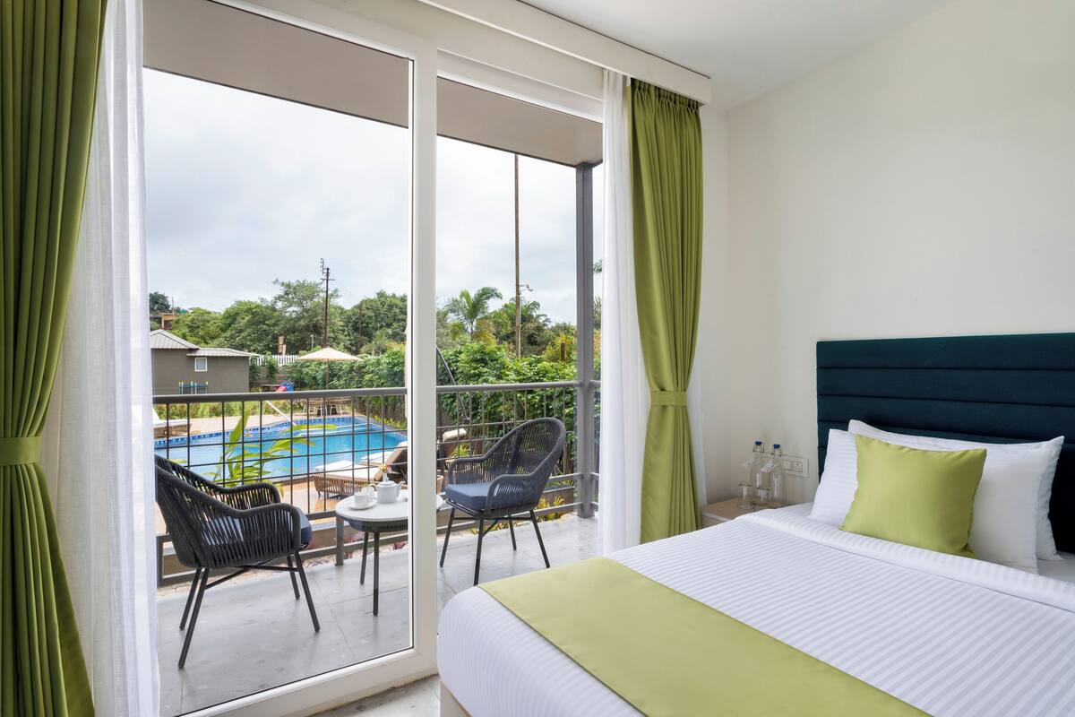 Habitación de hotel con cama, balcón y vistas a una piscina, además de mobiliario exterior.
