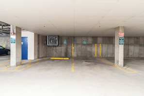 A parking garage with concrete pillars, yellow lines, and green signs indicating parking spots.