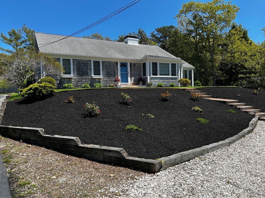 A house with a stone facade, a front porch, and a landscaped garden with a stone border.
