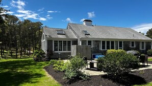 A two-story house with a sloped roof, a front porch, and a landscaped garden. - Steps to Red River Beach! (Harwich)