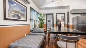 A compact room with a bed, a dining table with chairs, a refrigerator, and a potted plant. - HTX Ultra Chiic Suite #1 (Houston)