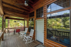 A wooden deck with rocking chairs and a table, large windows, and a door. - Charming & Rustic Cabin on the Little Red River! (Heber Springs)