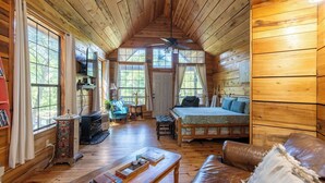 L’intérieur chaleureux d’un chalet avec un plafond en bois, un lit, un canapé et une table à manger.