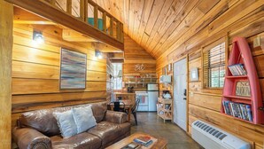 Un intérieur de chalet chaleureux, avec un revêtement en bois, un canapé en cuir, un coin repas et une cuisine.
