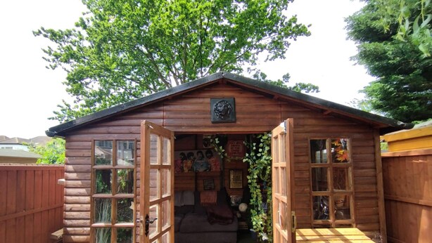 Une cabane en bois avec une véranda, un canapé et un petit jardin.