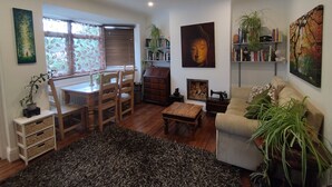 Un salon chaleureux comprenant un coin repas, un canapé, une table basse et une cheminée. Les murs sont ornés d’étagères à livres et d’un grand tableau représentant un Bouddha.