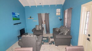 A living room with two sofas, a television, and a patterned rug. - Tao's Cozy Cottage! Piton View (Soufriere)