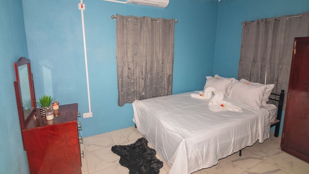 A bedroom with a bed, curtains, a mirror, a small plant, and a heater. - Tao's Cozy Cottage! Piton View (Soufriere)