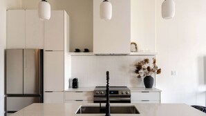 Une cuisine moderne avec des meubles blancs, un réfrigérateur en acier inoxydable, une cuisinière à gaz et des luminaires suspendus.