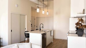 Une cuisine moderne dotée d’un îlot central, de luminaires suspendus et d’un lave-vaisselle encastré.