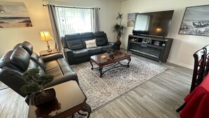 A living room with a leather sofa, a coffee table, a TV, and a bookshelf. - Golfer’s Dream Home (Haines City)