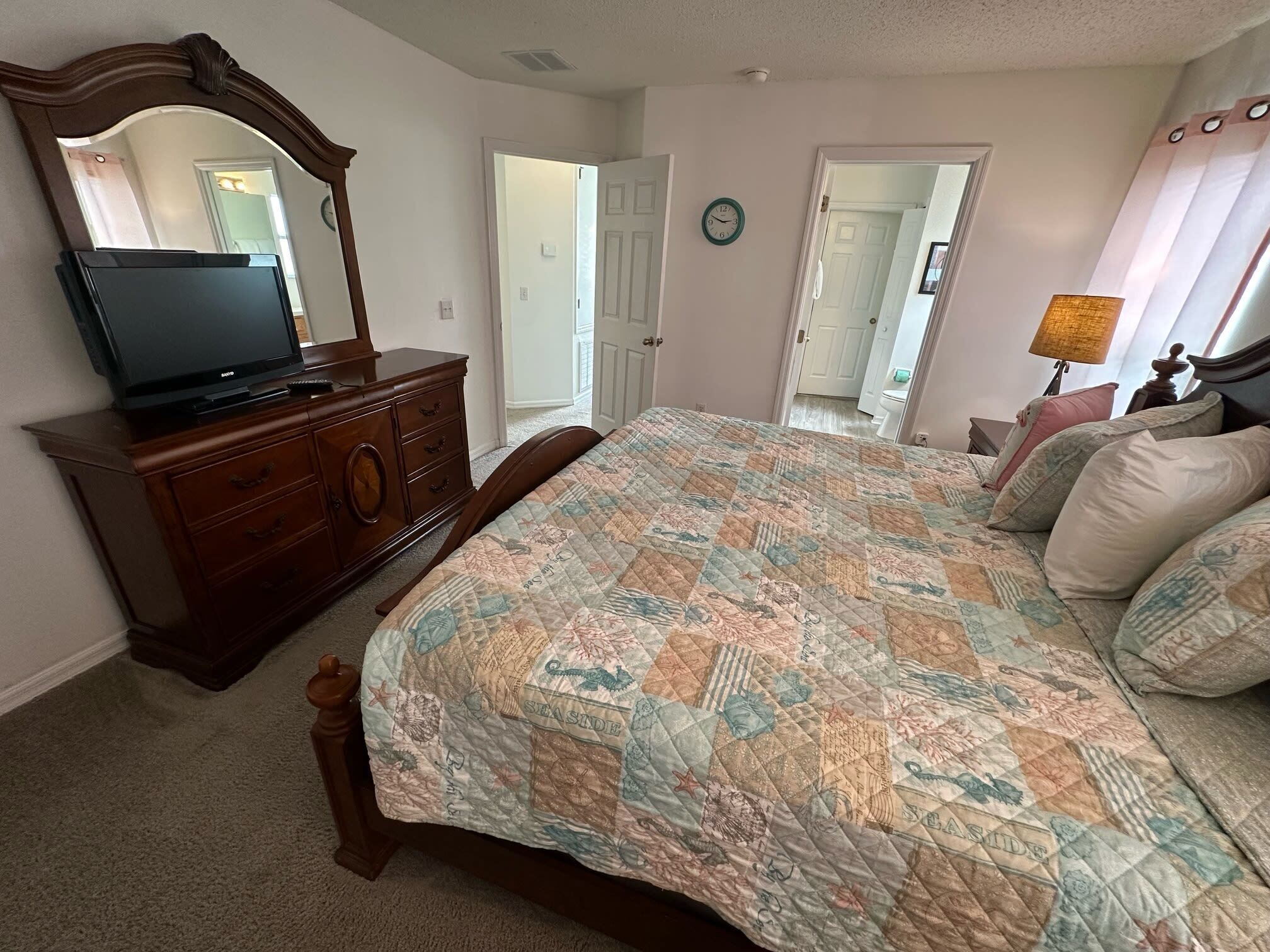 Une chambre à coucher avec un lit, une commode, une télévision et une horloge au mur.
