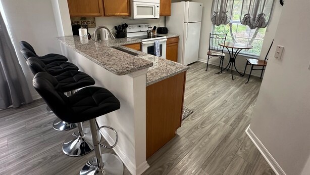 A modern kitchen with granite countertops, wooden cabinets, and a central island with bar stools. - Golfer’s Dream Home (Haines City)