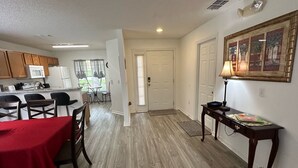 A spacious kitchen with wooden cabinets, a dining area with a red table, and a hallway leading to a door. - Golfer’s Dream Home (Haines City)