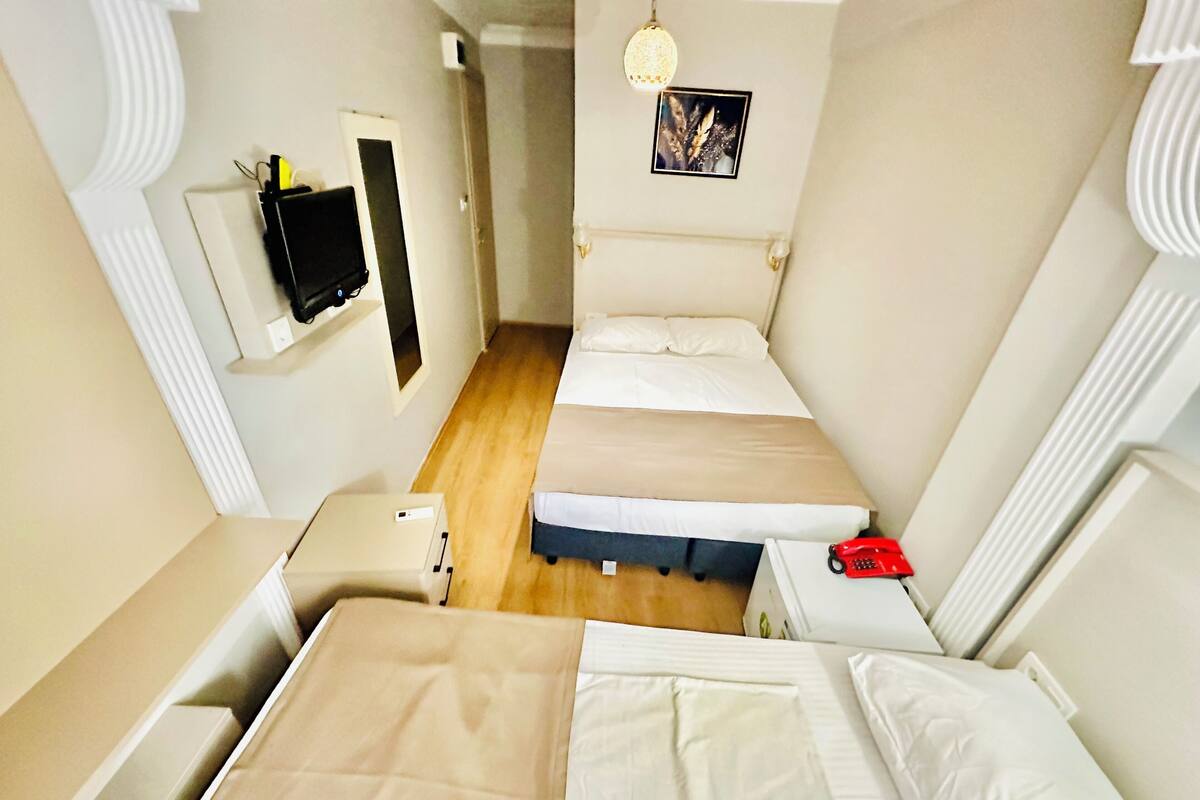A compact hotel room with two beds, a small bedside table, a red telephone, and a picture on the wall.
