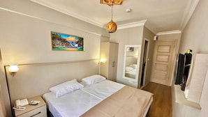 A hotel room with a bed, bedside table, lamp, painting, wardrobe, mirror, and a door. - Crowned Exclusive Hotel (Istanbul)