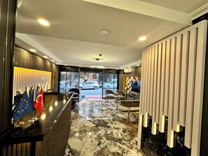 Un hall de hotel con mostrador de recepción, suelo de mármol y vistas a la calle.