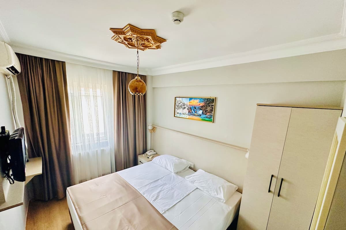 A hotel room with a bed, a wardrobe, a desk with a telephone, and a painting on the wall.