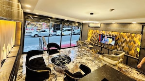 A hotel lobby with a marble floor, black and gold chairs, a TV on the wall, and a view of the street outside. - Crowned Exclusive Hotel (Istanbul)