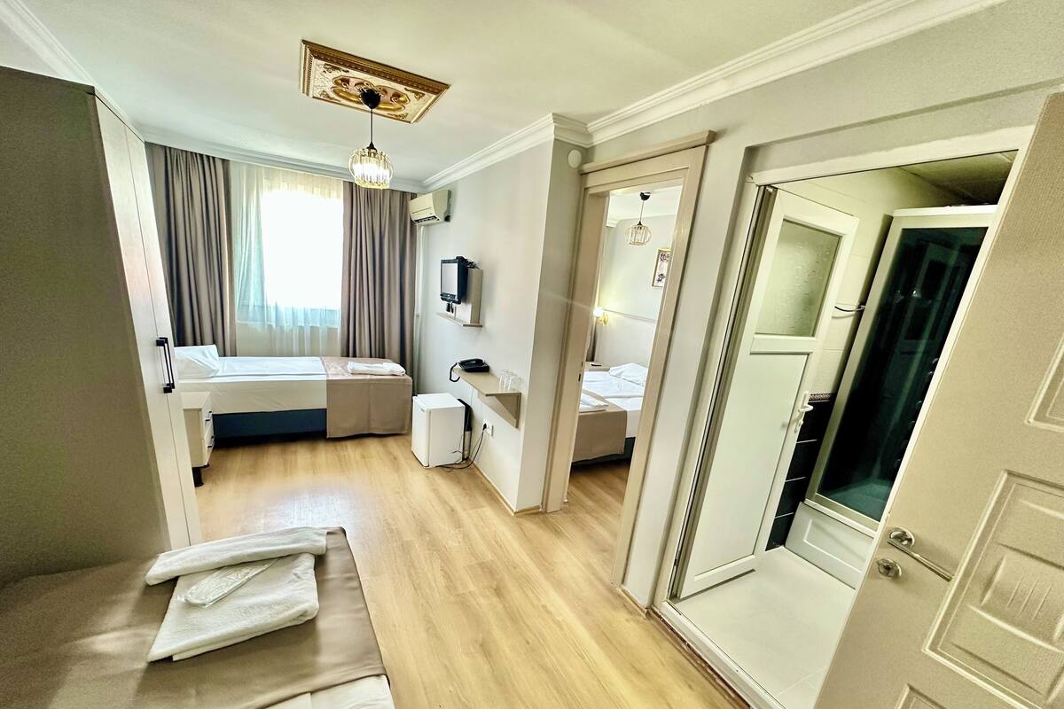 A hotel room with a bed, a desk, a chair, a small refrigerator, a vanity with a mirror, and a door leading to another room.