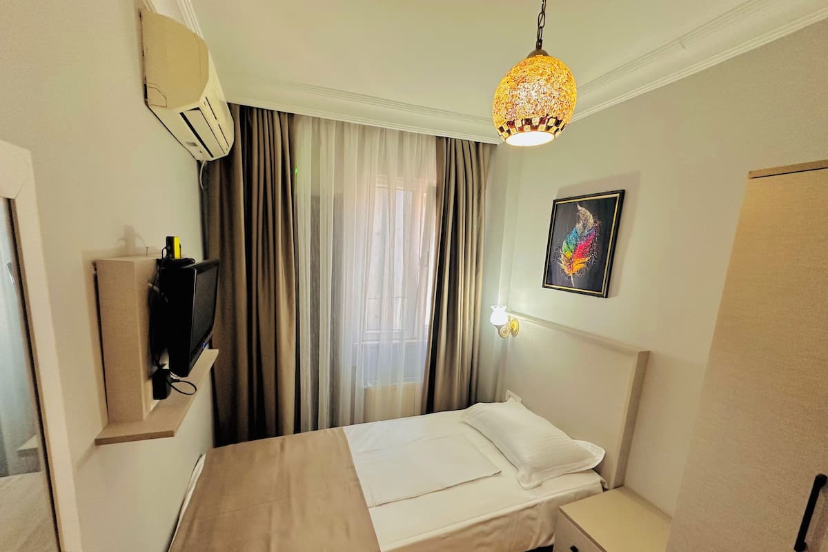 A hotel room with a bed, bedside table, wardrobe, air conditioning unit, and a decorative lamp.