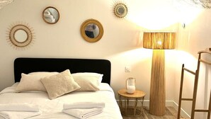 A bedroom with a black headboard, white bedding, and a round mirror on the wall. - Apartment Saint Germain des Pres Bon Marche (Paris)