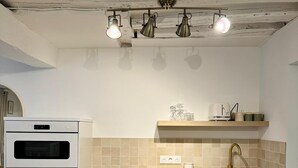 A kitchen with white cabinets, a wooden countertop, a built-in oven, a sink with a gold faucet, and a ceiling with exposed beams and pendant lights. - Apartment Saint Germain des Pres Bon Marche (Paris)