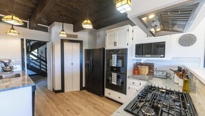 Une cuisine moderne avec un plancher en bois, des armoires blanches, un réfrigérateur noir, une cuisinière et des luminaires suspendus.