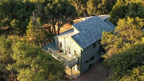 Une maison avec un toit en pente, une véranda et une vue sur les arbres et les montagnes environnants.