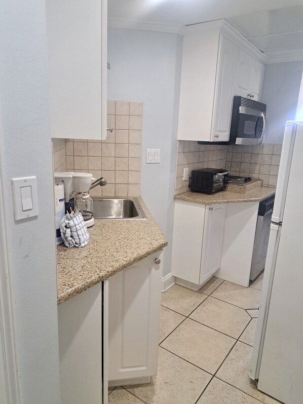 A compact kitchen with white cabinets, a stainless steel sink, a microwave, and a dishwasher.