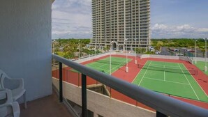 Un balcón con una cancha de tenis y un edificio alto al fondo.