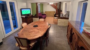 Een eetgedeelte met een houten tafel en stoelen, een televisie en een bank op de achtergrond.