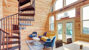 Ein Holzblock-Interieur mit Wendeltreppe, einer Couch, einem Esstisch und großen Fenstern.