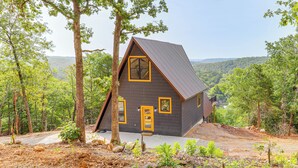 Eine Holzhütte mit geneigtem Dach, umgeben von Bäumen und einer bewaldeten Landschaft.
