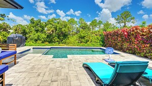 A swimming pool with a tiled deck, lounge chairs, and a covered grill area.