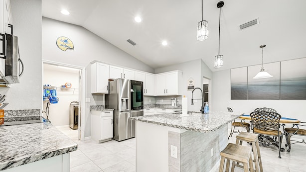 A modern kitchen with white cabinets, a granite countertop, stainless steel appliances, and a dining area with a wooden table and chairs.